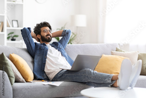 Happy indian man in casual wear reclining on sofa with his laptop