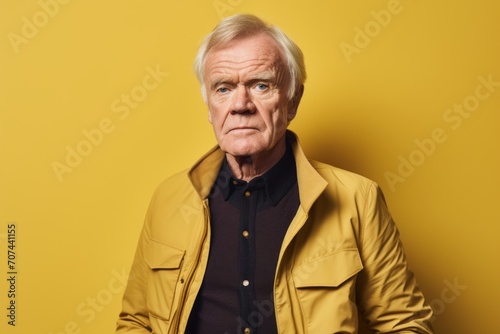 Portrait of an elderly man in a yellow jacket on a yellow background © Inigo