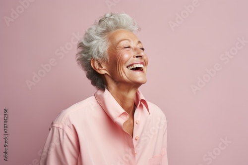 Portrait of a happy senior woman laughing and looking up on a pink background