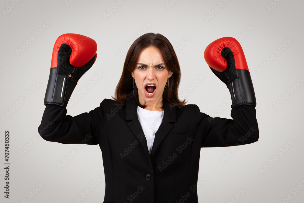 Confident strong young European lady winner in suit, boxing gloves rise fists, scream