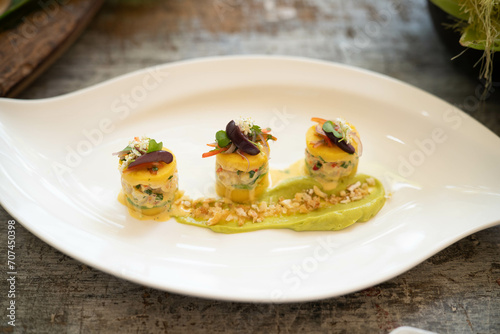 three small peruvian potato cakes called causa limeña - with chicken avocado onion peppers and flower garnish at fine dining restaurant