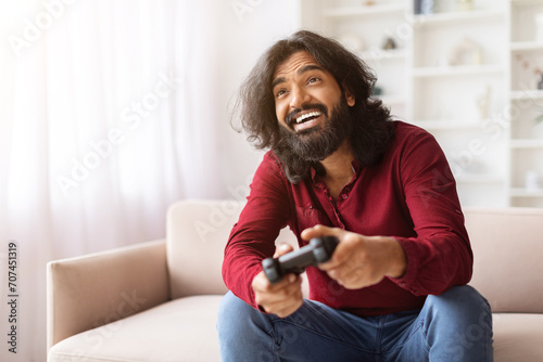 Emotional eastern guy playing video game with joystick at home photo