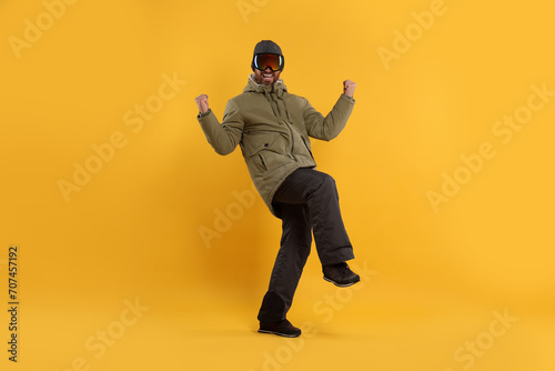 Winter sports. Cheerful man in ski suit and goggles on orange background