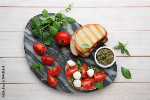 Delicious Caprese sandwich with mozzarella, tomatoes, basil and pesto sauce on white wooden table, top view