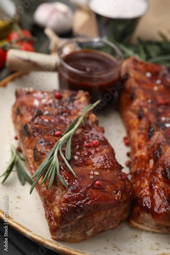 Tasty roasted pork ribs served with sauce and rosemary on table, closeup
