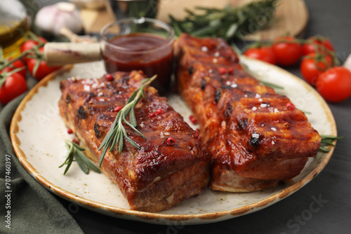 Tasty roasted pork ribs served with sauce and rosemary on grey wooden table, closeup