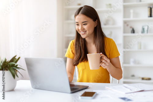 Young Smiling Asian Freelancer Woman Using Laptop And Drinking Coffee At Home