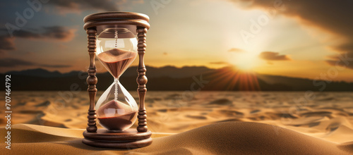 A classic hourglass with sand sifting through its narrow passage, symbolising the relentless march of time amidst desert dunes and sunset time photo