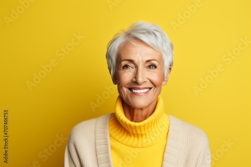 Happy senior woman in yellow sweater and scarf looking at camera over yellow background