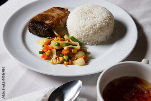 pieces of grilled tuna served on a plate with rice, chili sauce and fresh vegetables