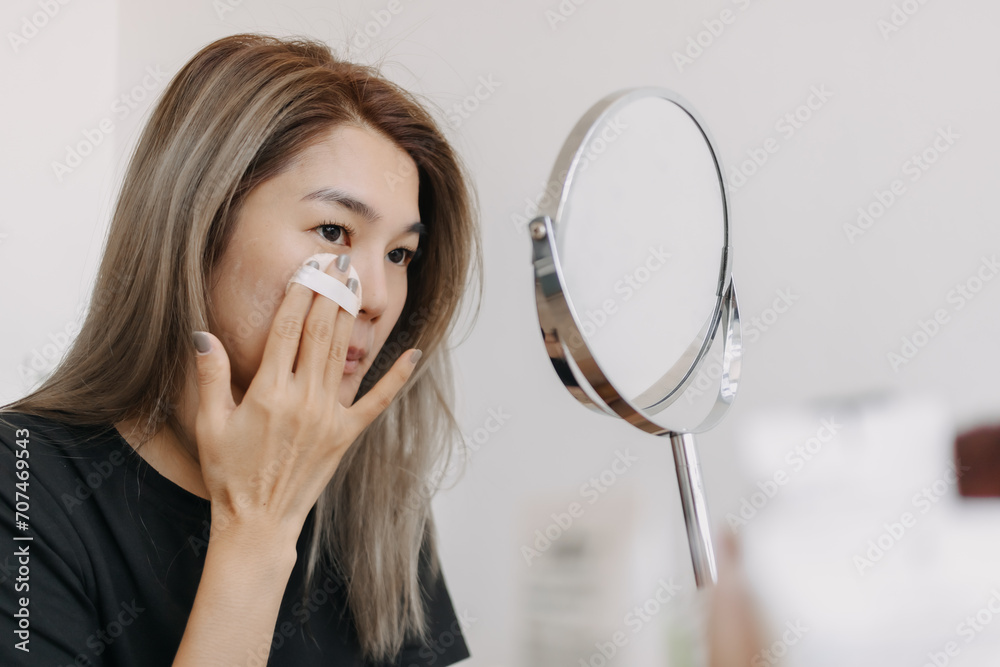 Asian woman wearing make up in front of the mirror in white bright room. Asian woman wearing make up in front of the mirror in white bright room.