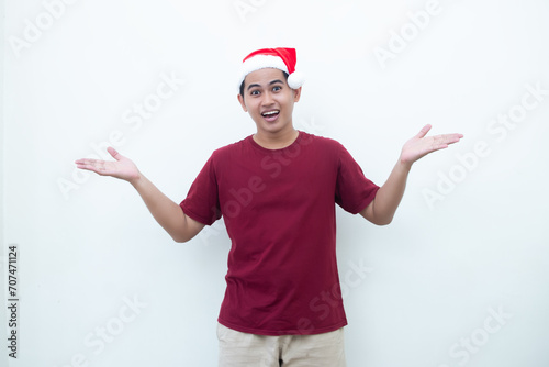 Young Asian man wearing a Santa Claus hat smiling, shock and pointing to her side isolated by white background for visual communication