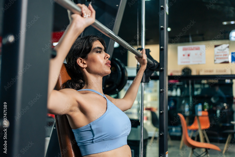 Caucasian young sportswoman lift up weight machine or barbell in gym.