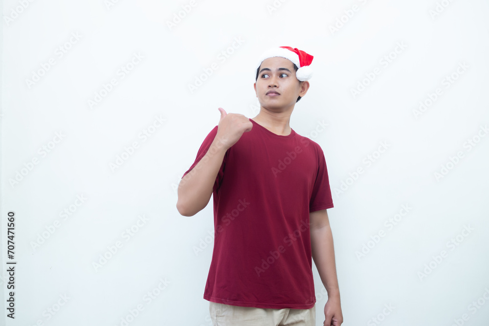 Young Asian man wearing a Santa Claus hat smiling, shock and pointing to her side isolated by white background for visual communication