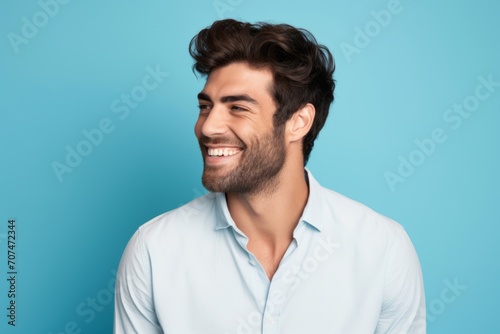 Handsome young man in shirt smiling and looking at camera on blue background © Inigo