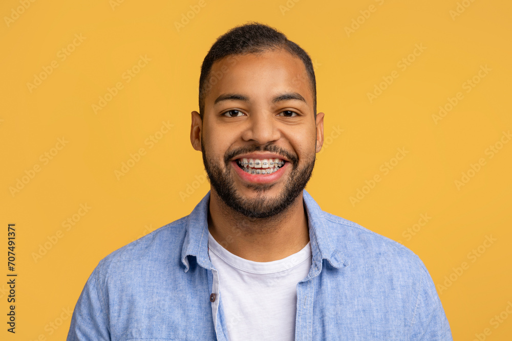 Cheerful young black man with dental braces posing against yellow background - obrazy, fototapety, plakaty 