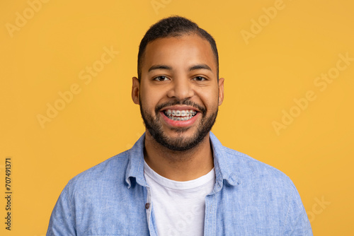 Cheerful young black man with dental braces posing against yellow background photo