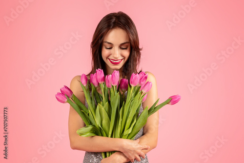 Admiring woman in a sequined dress smiles gently at a large bouquet of pink tulips #707507773