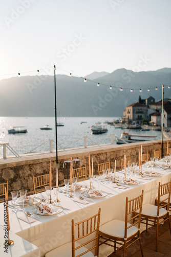 Long festive set table with candles stands on the terrace by the sea