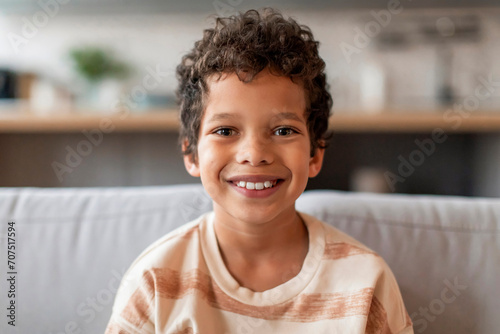 Cheerful black boy with curly hair and bright smile looking at camera photo