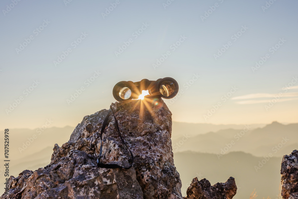 binoculars on top of rock mountain at beautiful sunset background.