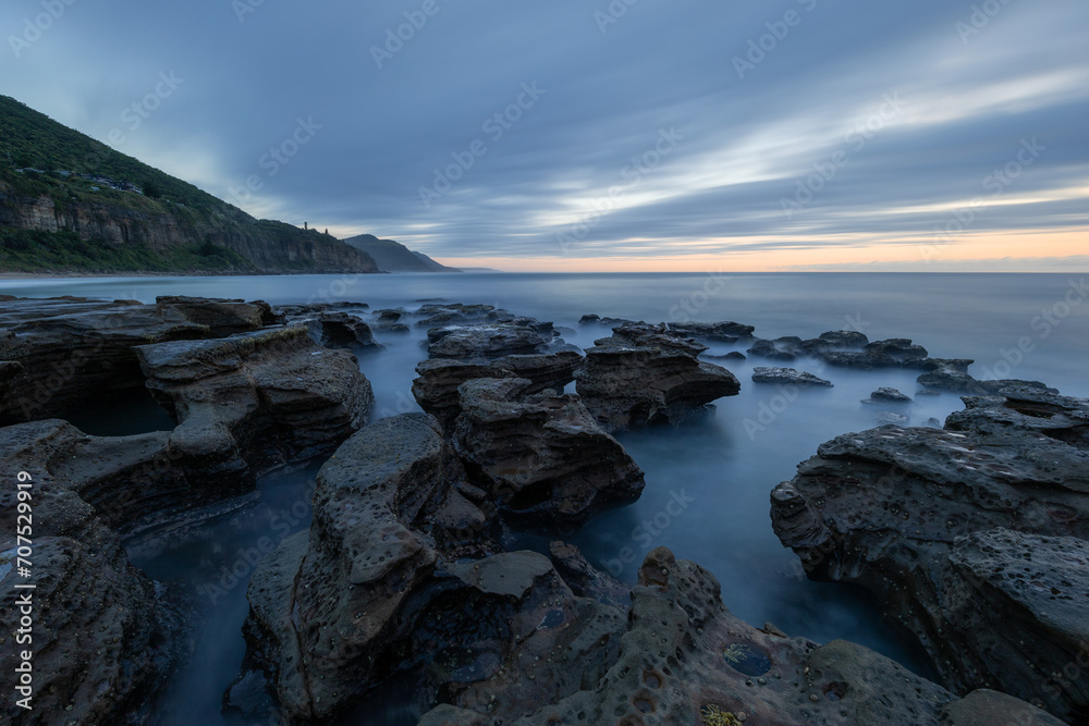 Long exposure view of rocky shore with cloudy sky.