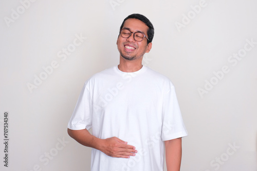 Adult Asian man smiling happy with one hand touching his stomach photo