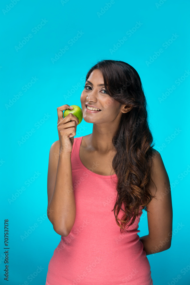 Happy Indian Woman holding an apple on blue background. Happy Indian Woman holding an apple on blue background.
