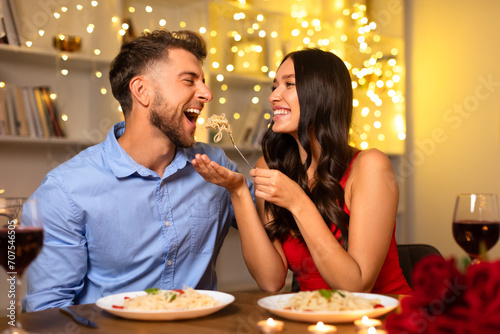 Couple sharing a playful moment with pasta during romantic dinner