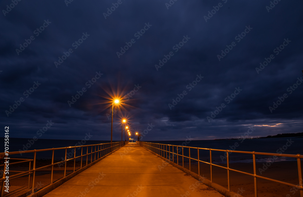 Perspective view of a jetty with railings and starburst lights at dawn on a tropical beach in tropical Queensland, Australia.