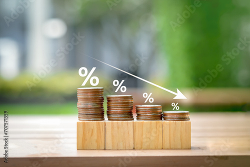 Low interest rates. Percentage sign on different high of coins stack and arrow going down. Business and financial banking, reducing interest rates payment, mortgage rate, loan and tax concept. photo