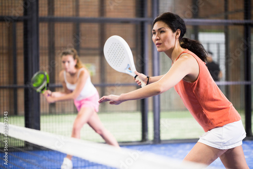Portrait of concentrated asian woman playing paddle tennis indoors, preparing to hit forehand to return ball.