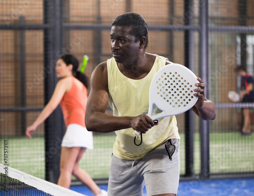 Portrait of sporty African American hitting backhand during paddle tennis friendly match in close court