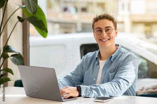 Smiling proud millennial european guy student in glasses, typing on computer photo