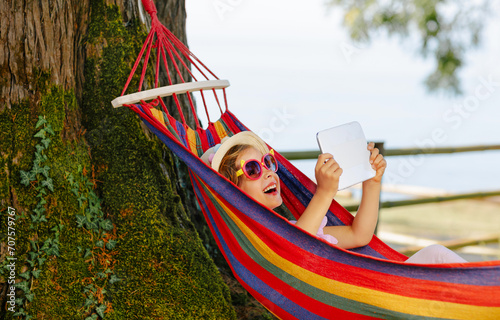 A child swings in a bright hammock outdoors. A child consumes entertainment content from gadgets in nature. Gadget addiction in children and adolescents.