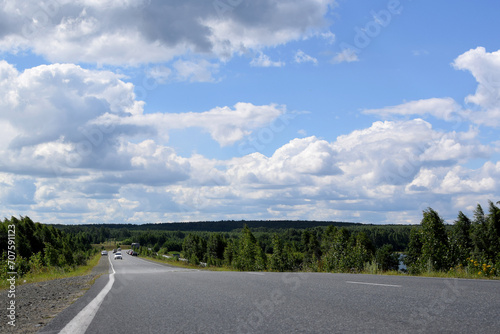 Beautiful dense forest along the highway. Summer landscape, white clouds on a blue sky.