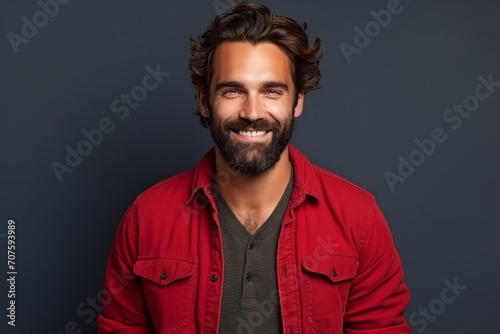 Portrait of a handsome young man with beard and mustache smiling at the camera while standing against grey background