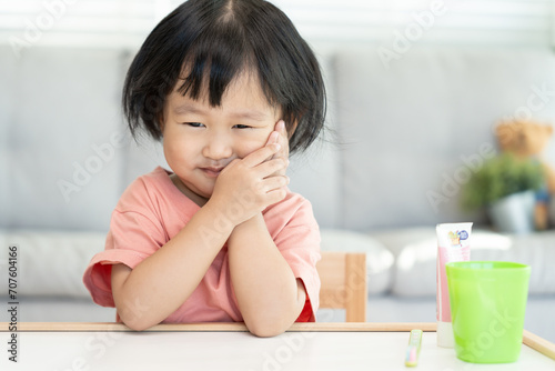 little asian girl presses hand to cheek, suffers from pain in tooth. Teeth decay, dental problems, child emotions and facial expression, oral health care, reducing sweets, fluorine coating