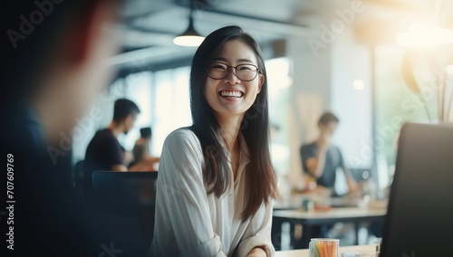 Young Asian woman with glasses smiling  seated in a bright office.