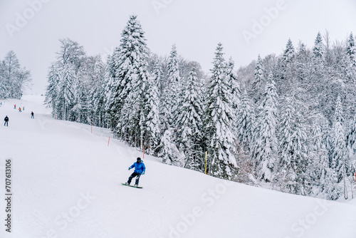 Snowboarder in a blue ski suit rides along a hilly snowy slope along the forest