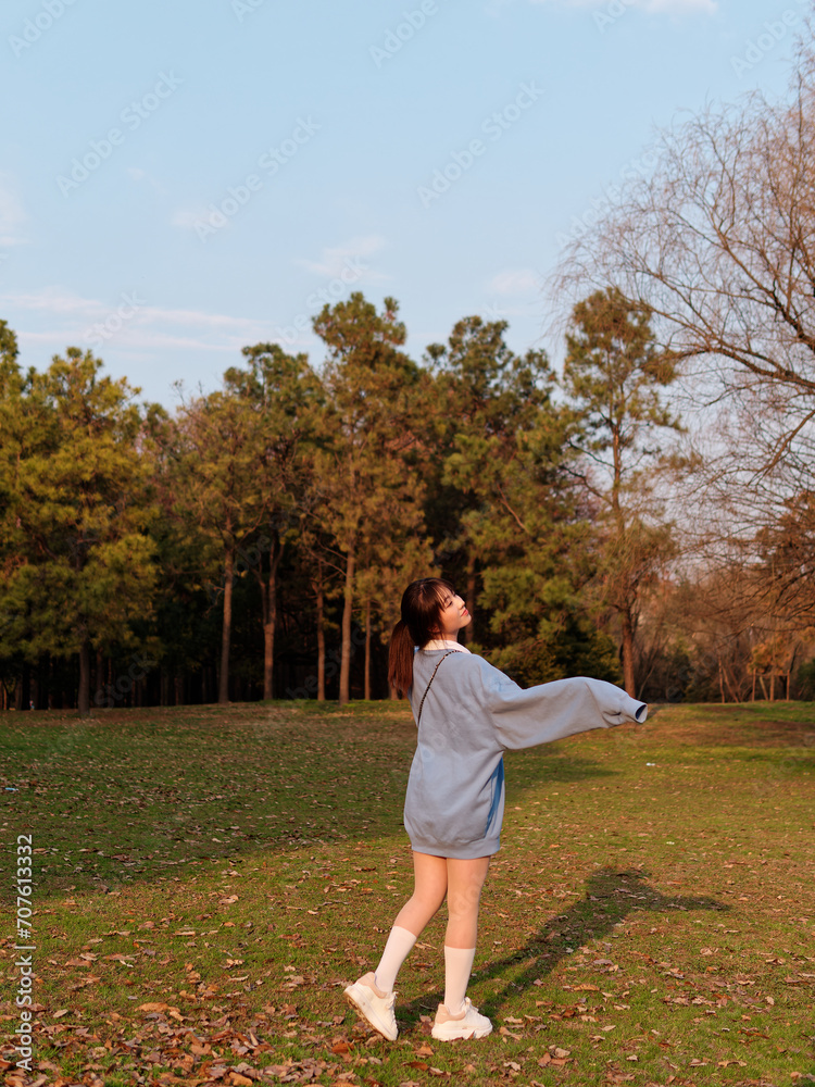 Beautiful young Chinese woman dancing with joy in sunny summer forest, wearing blue loose oversized top, mini skirt and white shoes. Emotions, people, beauty, youth and lifestyle portrait.