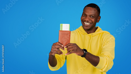 A radiant Black man in a yellow hoodie beams while holding his passport and boarding pass #707616187