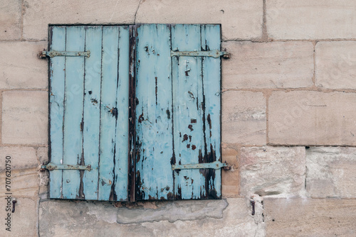 Cement stone wall with window and old damaged wooden shutter, painted in blue, no person