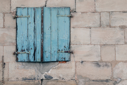 Sandstone brick wall with window and old wooden shutter, painted in pastel blue, no person