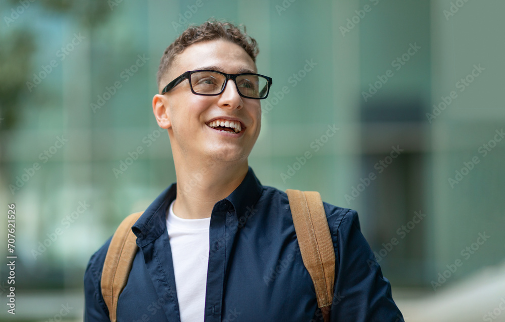 Cheerful student with glasses and a backpack looking up and smiling