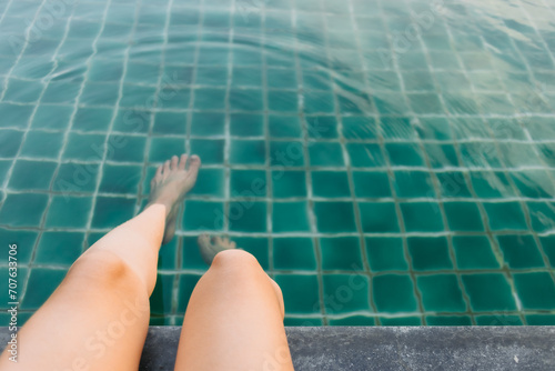 Photo of woman legs sitting at swimming pool, kicking water, soaking feet in pool.
