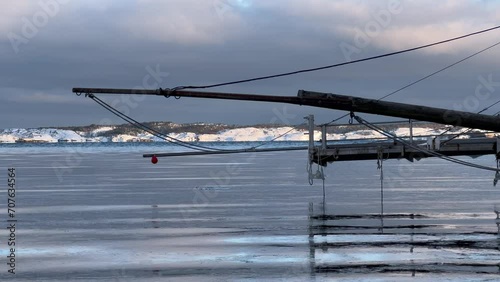 Calm winter coast in Norway, captured in smooth slow motion and 4K clarity. Snow meets blue water in a simple, peaceful scene. Boat pier in hanging over cold water. photo