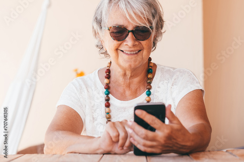 Attractive senior woman typing message on smartphone and smiling. Mature elderly woman enjoying tech and social