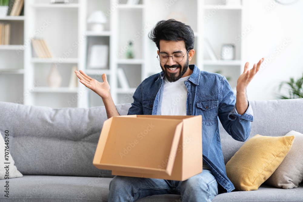Indian man expressing surprise and joy when opening cardboard package at home Indian man expressing surprise and joy when opening cardboard package at home