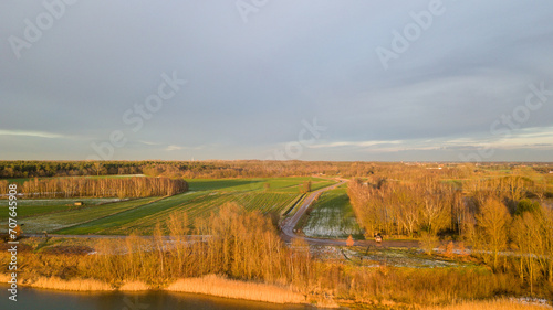 This aerial image captures a rural landscape bathed in the warm glow of a setting sun. A winding road cuts through the scene  leading towards the horizon  flanked by fields in various states of use